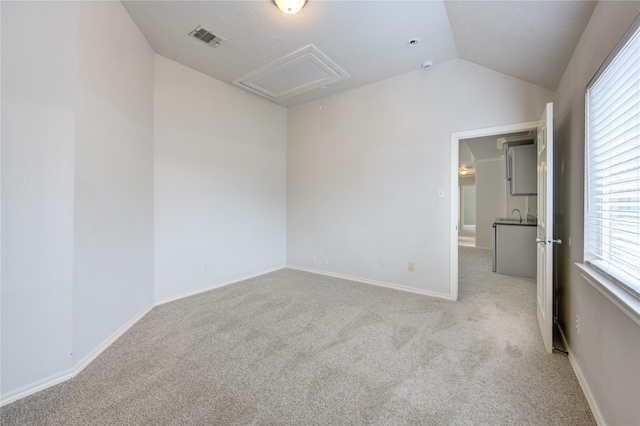 unfurnished room with vaulted ceiling, visible vents, light carpet, a sink, and attic access