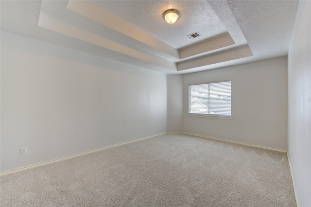 unfurnished room with a raised ceiling, carpet floors, visible vents, and a textured ceiling