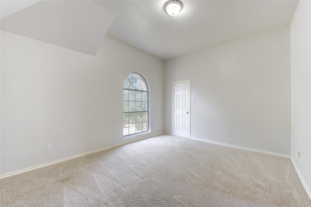 empty room featuring carpet, a textured ceiling, lofted ceiling, and baseboards