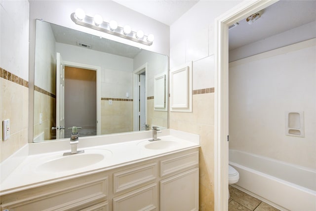 full bathroom with toilet, a sink, double vanity, and tile walls