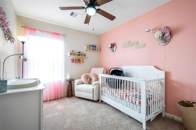 carpeted bedroom with visible vents, a crib, and ceiling fan