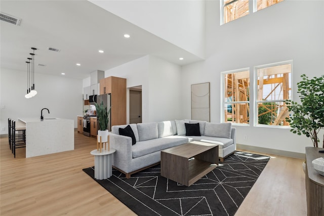 living room featuring a high ceiling, light wood-style floors, visible vents, and recessed lighting