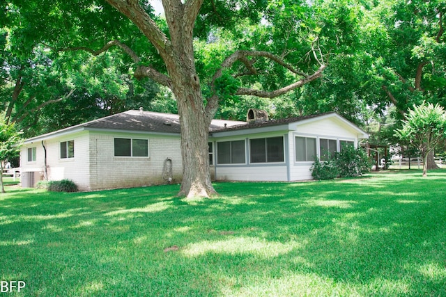 rear view of house with a sunroom, central air condition unit, a yard, and a chimney