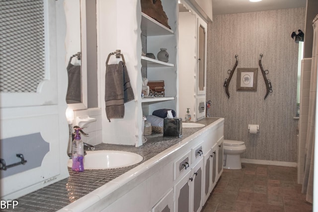 bathroom with a sink, baseboards, toilet, and double vanity