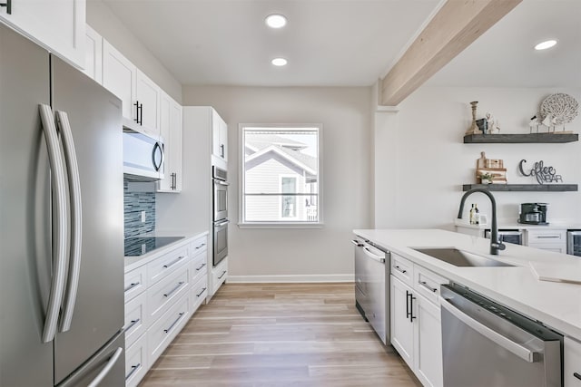kitchen featuring appliances with stainless steel finishes, a sink, light countertops, white cabinets, and light wood-style floors