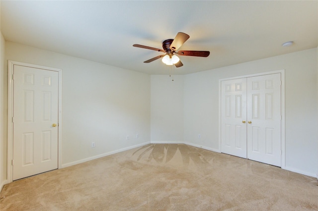 empty room featuring light colored carpet, a ceiling fan, and baseboards