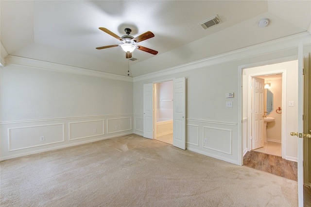 unfurnished bedroom featuring visible vents, a decorative wall, light carpet, a tray ceiling, and ensuite bath