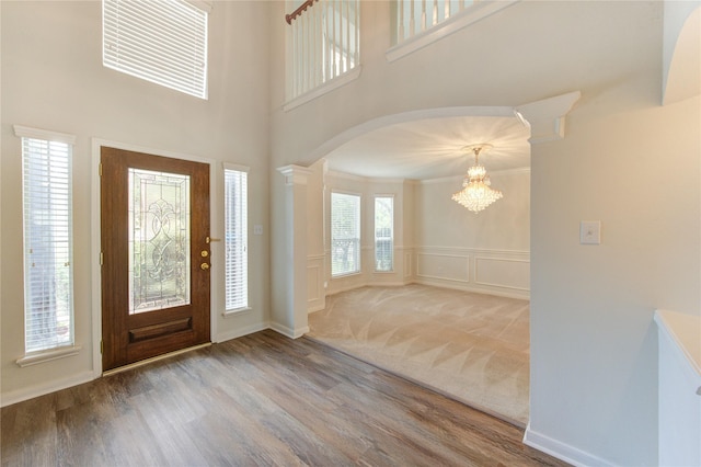 foyer with arched walkways, wood finished floors, an inviting chandelier, a decorative wall, and ornate columns