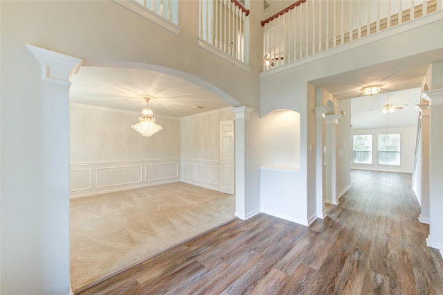 empty room with arched walkways, decorative columns, ceiling fan with notable chandelier, and wood finished floors