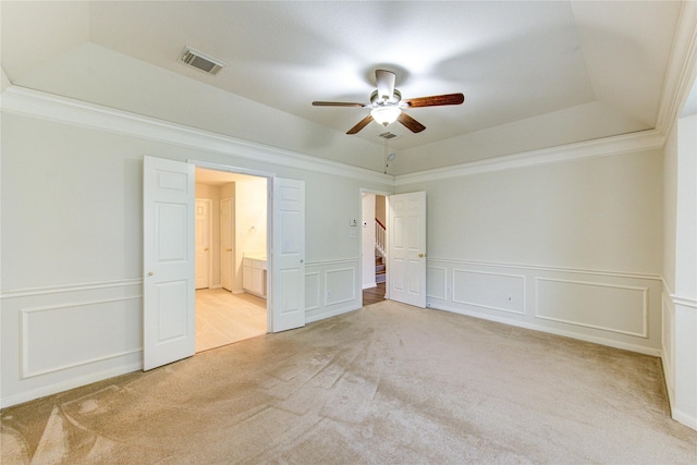 unfurnished bedroom featuring crown molding, a tray ceiling, light colored carpet, and a decorative wall