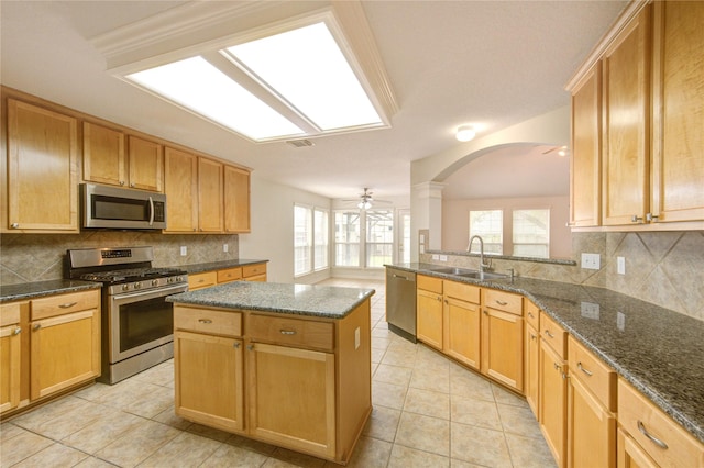 kitchen featuring a ceiling fan, appliances with stainless steel finishes, tasteful backsplash, arched walkways, and a sink