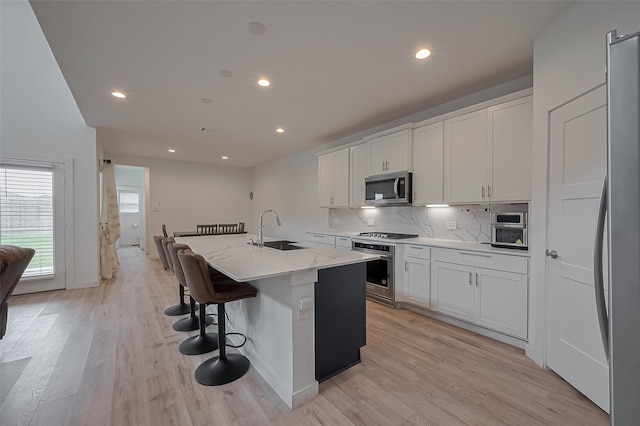 kitchen with white cabinets, stainless steel appliances, a sink, tasteful backsplash, and an island with sink