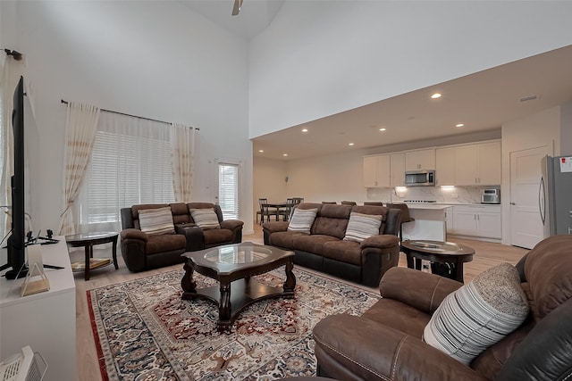living room featuring recessed lighting, a towering ceiling, visible vents, and light wood-type flooring