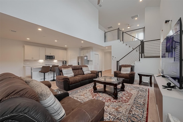 living area with recessed lighting, stairway, a high ceiling, visible vents, and light wood-style flooring