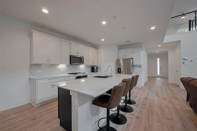 kitchen with white cabinets, stainless steel appliances, a sink, backsplash, and light wood-style floors