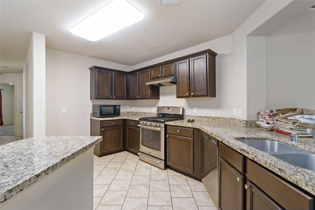 7218 Alava Dr, Magnolia, TX 77354 - kitchen with appliances with stainless steel finishes, under cabinet range hood, a sink, light tile patterned floors, and dark brown cabinetry