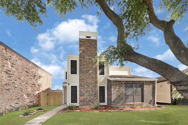 view of front of property featuring brick siding, a chimney, fence, and a front yard