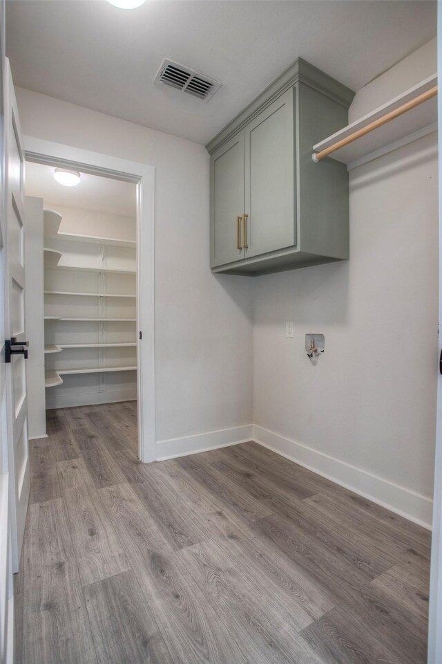 clothes washing area featuring hookup for a washing machine, wood finished floors, cabinet space, baseboards, and visible vents