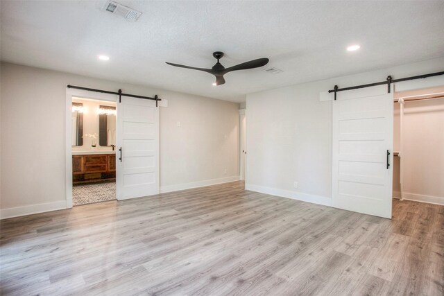 unfurnished bedroom featuring a barn door, light wood finished floors, visible vents, and recessed lighting