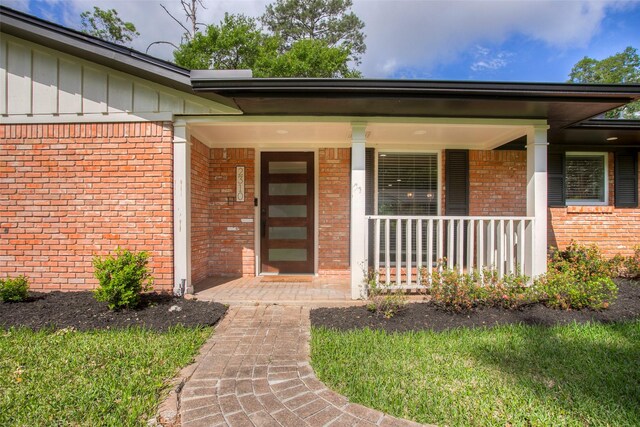 doorway to property with brick siding, board and batten siding, and covered porch