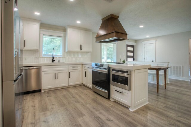 kitchen featuring island exhaust hood, stainless steel appliances, a sink, a peninsula, and light wood-style flooring