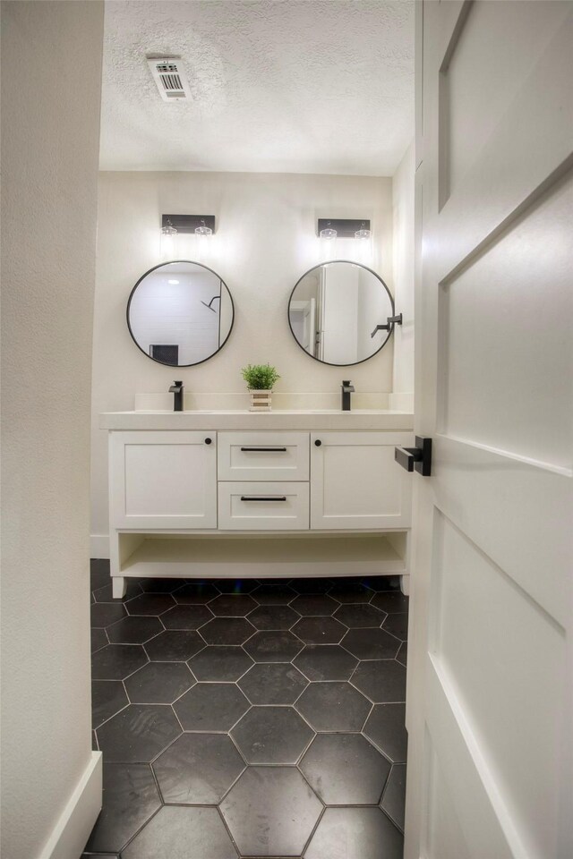full bathroom with a sink, tile patterned floors, a textured ceiling, double vanity, and visible vents