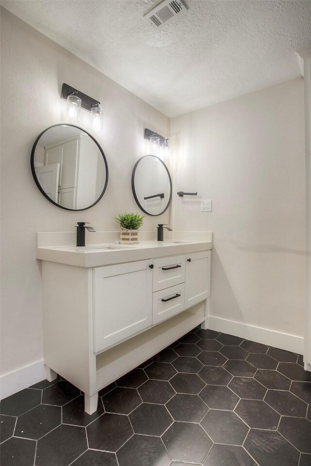 bathroom with baseboards, double vanity, visible vents, and a textured ceiling
