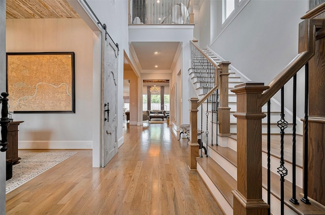 foyer entrance with a barn door, baseboards, wood finished floors, stairway, and ornamental molding