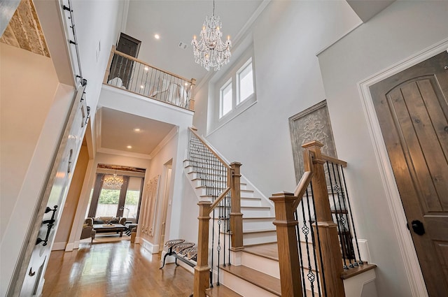 foyer featuring a chandelier, a towering ceiling, stairway, wood finished floors, and crown molding