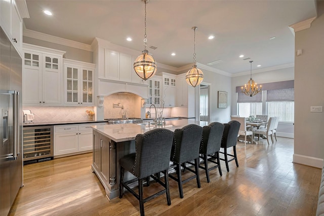 kitchen featuring wine cooler, a chandelier, tasteful backsplash, stainless steel built in fridge, and an island with sink