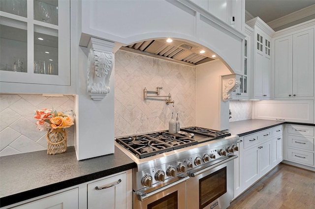 kitchen featuring double oven range, backsplash, dark countertops, arched walkways, and crown molding