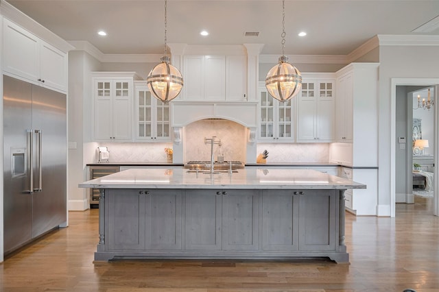 kitchen featuring stainless steel built in refrigerator, a chandelier, white cabinetry, crown molding, and a kitchen island with sink