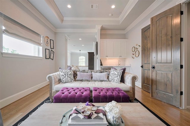 living area featuring a tray ceiling, light wood-style flooring, baseboards, crown molding, and recessed lighting