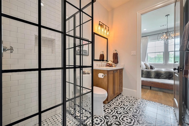 ensuite bathroom featuring toilet, tiled shower, a chandelier, and baseboards