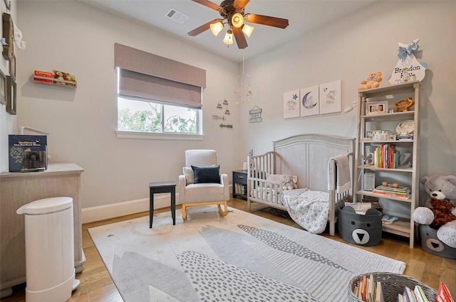 bedroom with wood finished floors, a nursery area, baseboards, and ceiling fan