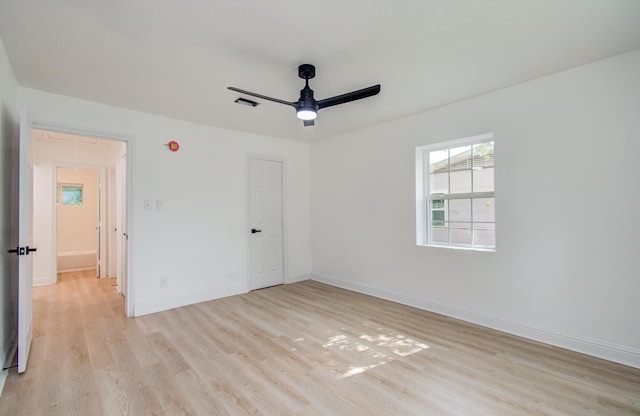 empty room with light wood finished floors, attic access, baseboards, visible vents, and ceiling fan