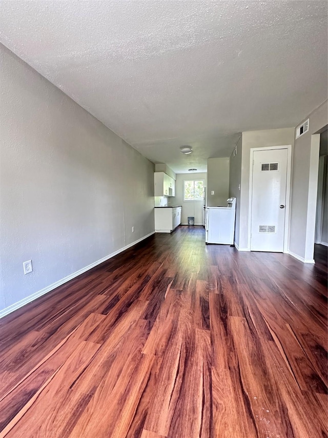 unfurnished living room featuring a textured ceiling, baseboards, visible vents, and dark wood-style floors