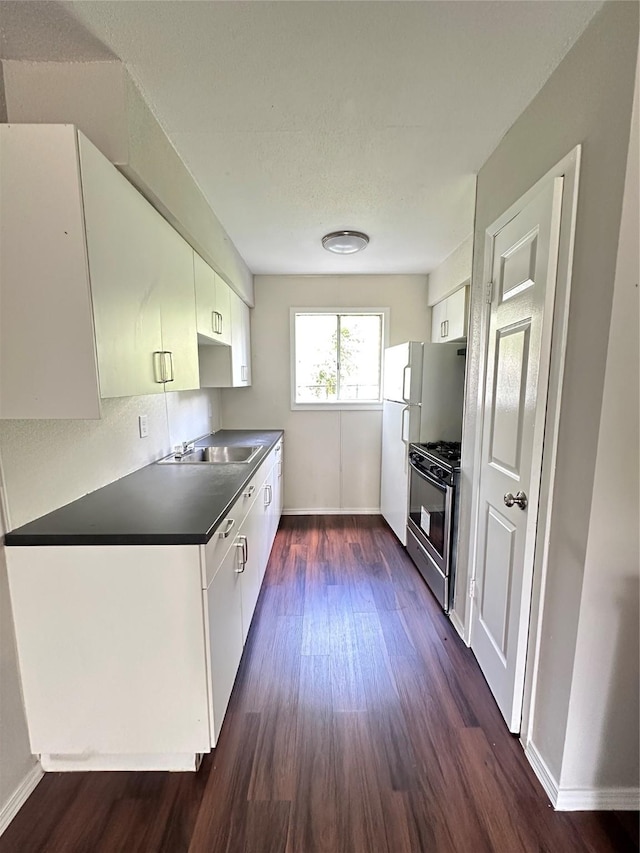 kitchen featuring gas range, white cabinets, dark countertops, and dark wood-type flooring