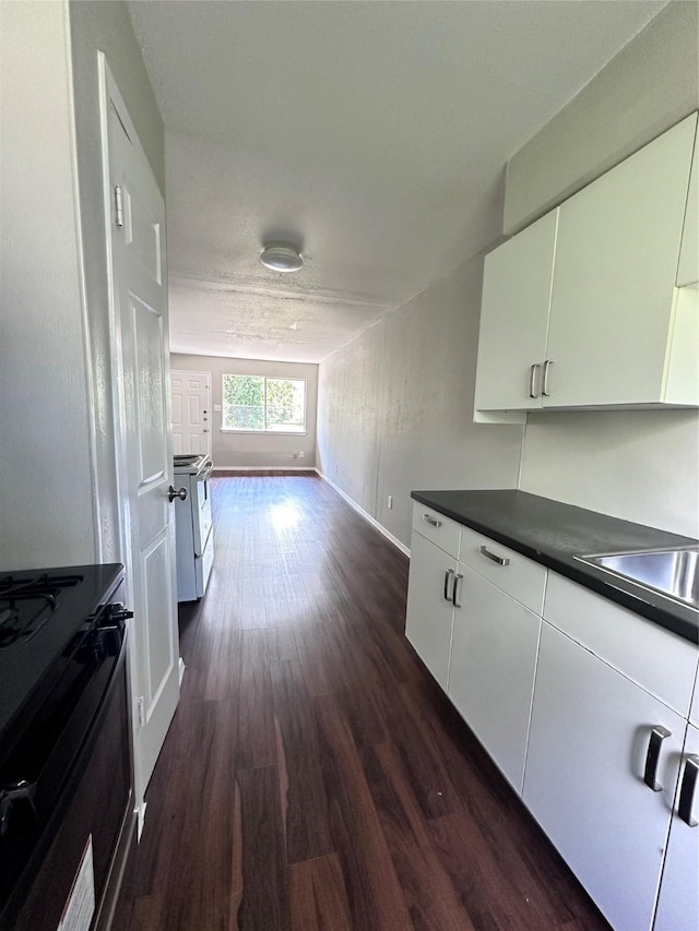kitchen featuring white cabinets, dark countertops, dark wood-style floors, and range