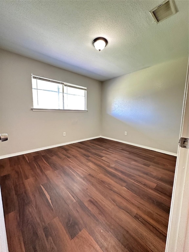 spare room with baseboards, dark wood-style flooring, a textured ceiling, and visible vents