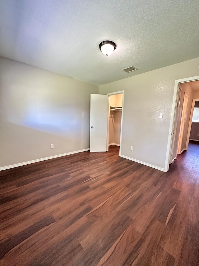 unfurnished bedroom with a closet, a spacious closet, baseboards, dark wood-style flooring, and visible vents