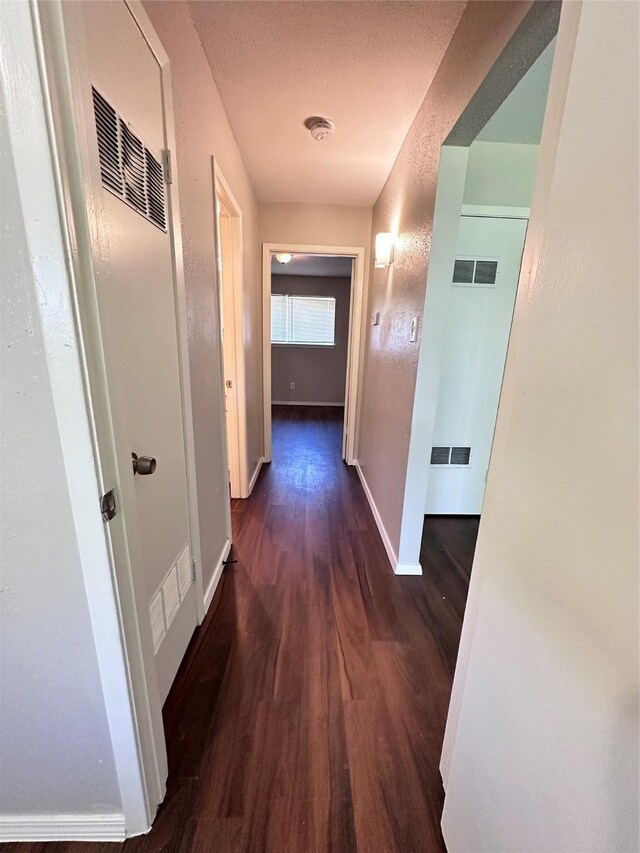 hall featuring wood finished floors, visible vents, and baseboards