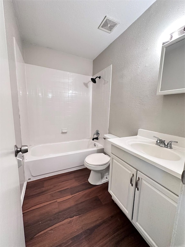 bathroom featuring toilet, visible vents, wood finished floors, a textured wall, and tub / shower combination