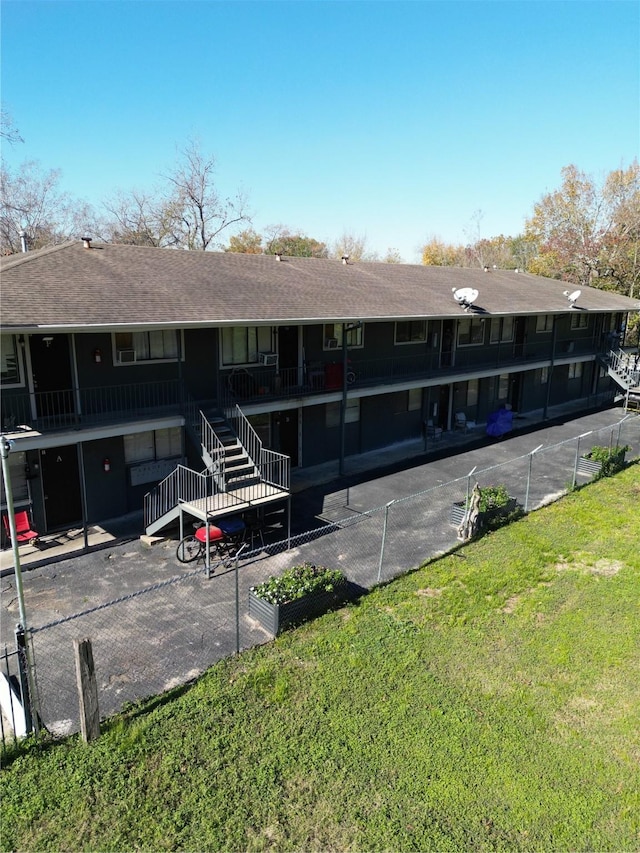 back of property with stairway, fence, a yard, and a shingled roof