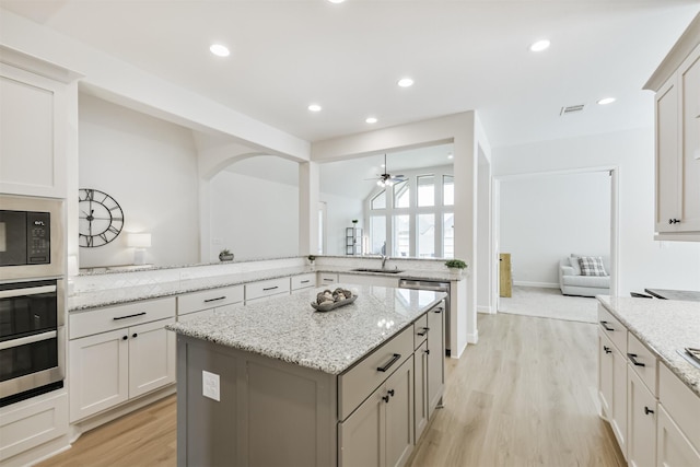kitchen with light wood finished floors, light stone countertops, a kitchen island, and a ceiling fan
