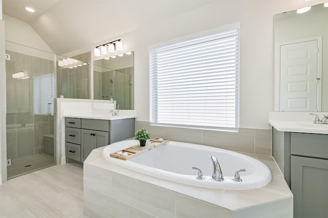 bathroom with vaulted ceiling, a garden tub, two vanities, and a stall shower