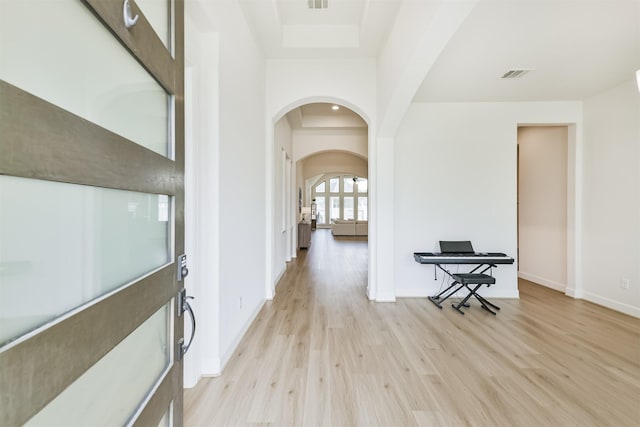 foyer entrance with baseboards, visible vents, arched walkways, and light wood-style floors