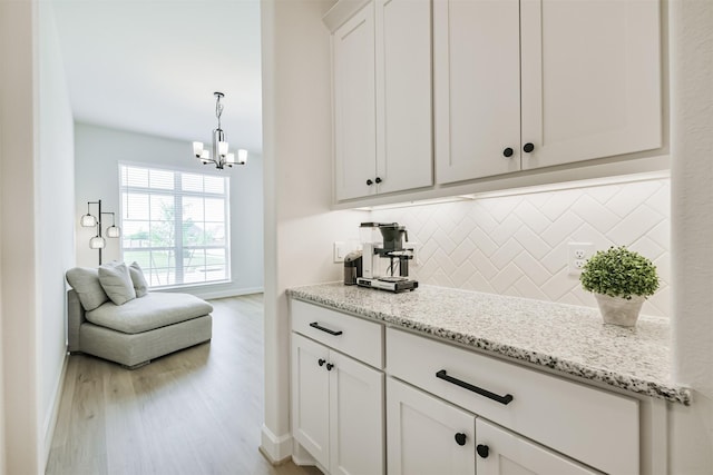bar featuring light wood finished floors, a chandelier, baseboards, and backsplash