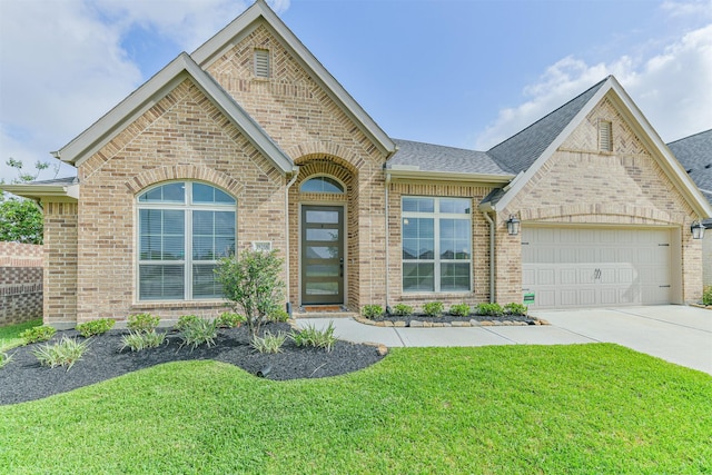 french provincial home featuring roof with shingles, a front lawn, concrete driveway, brick siding, and an attached garage