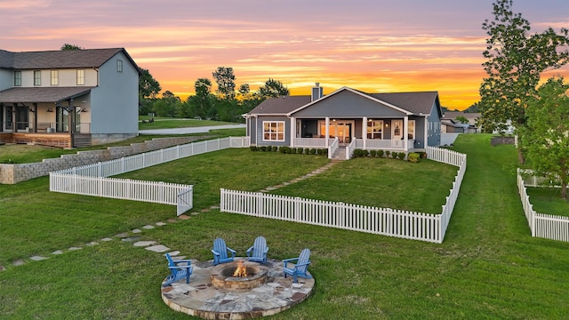 254 Peninsula Dr, Livingston, TX 77351 - back of house at dusk featuring a fenced backyard, a fire pit, a porch, a chimney, and a lawn